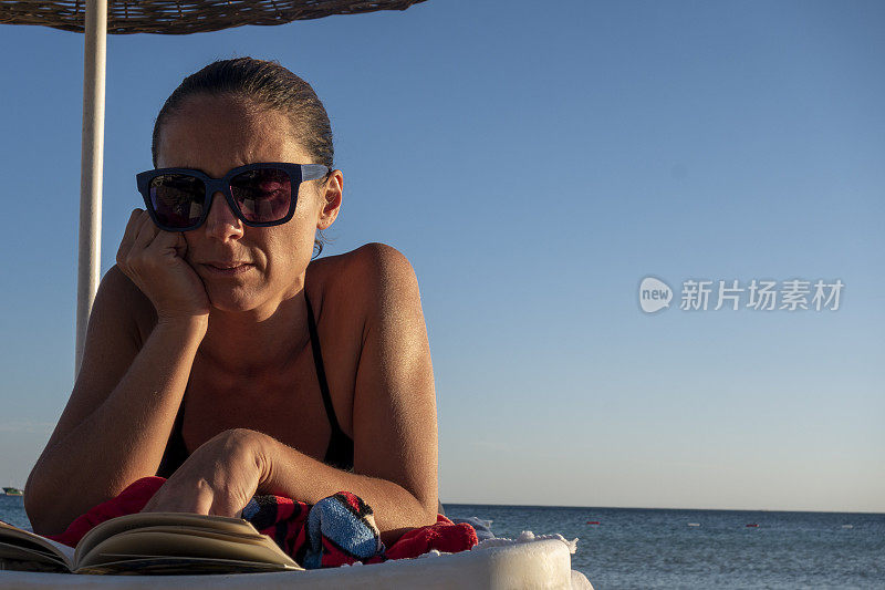 美丽的女人正在沙滩上的日光浴床上看书