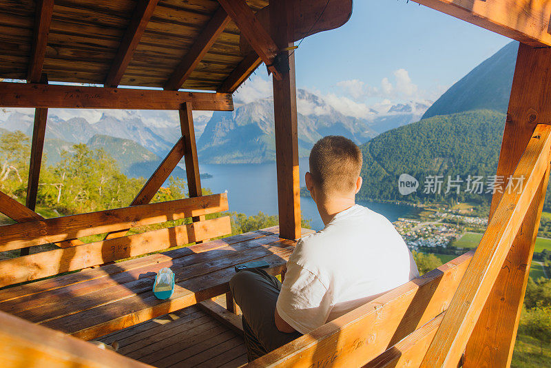 一名旅行者坐在山间小屋，欣赏挪威峡湾的美景