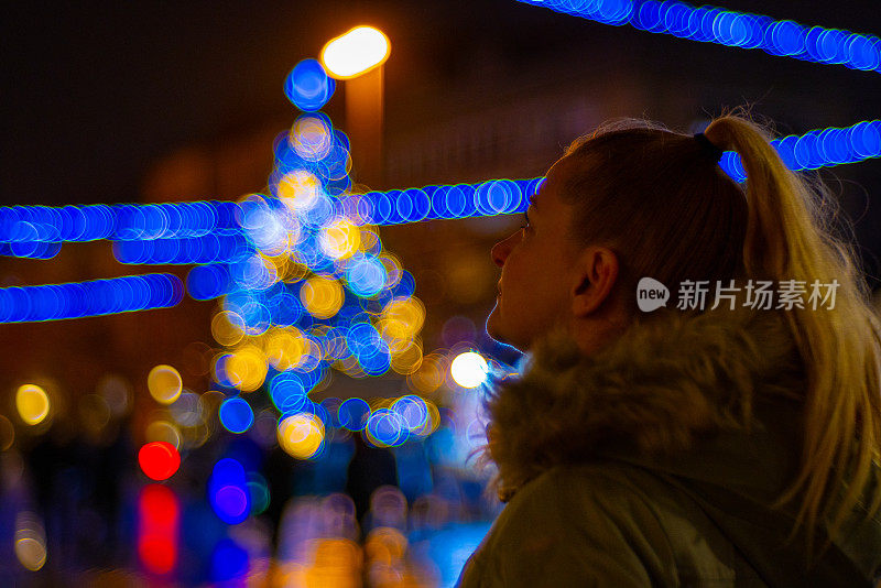 一名女子在夜晚欣赏被照亮的散焦圣诞装饰。马里博尔、斯洛文尼亚