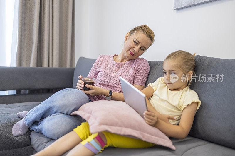 一名妇女与使用数码平板电脑的女儿一起休息