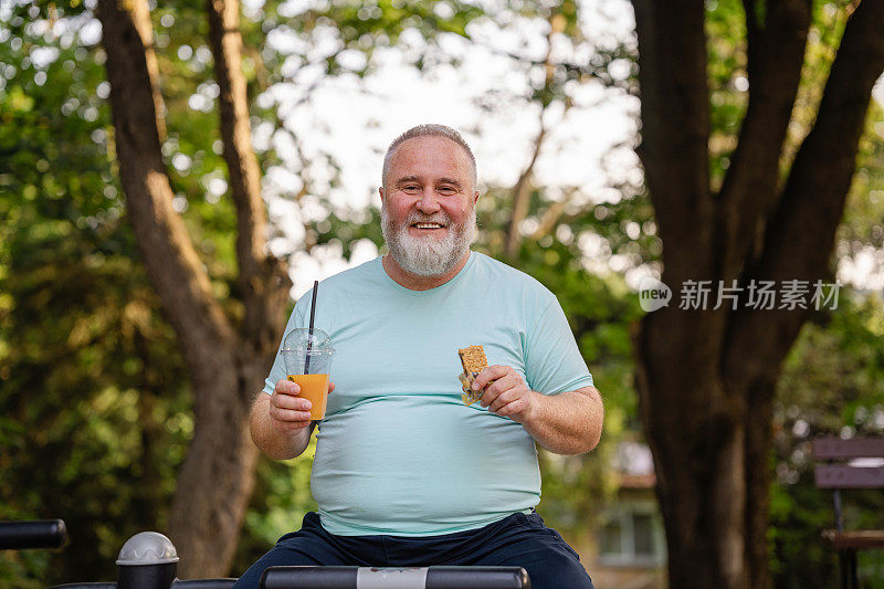 身体积极超重的男子肖像与冰沙和格兰诺拉燕麦棒在户外健身房