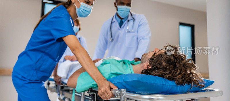 一群不同的医生在医院里移动重伤病人。有魅力的专业医护人员匆忙地将躺在担架上的急诊病人抬进手术室。