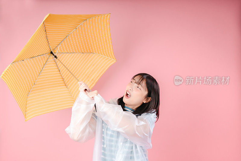一个兴奋的女孩穿着雨衣，在粉红色的背景上撑着一把开着的伞