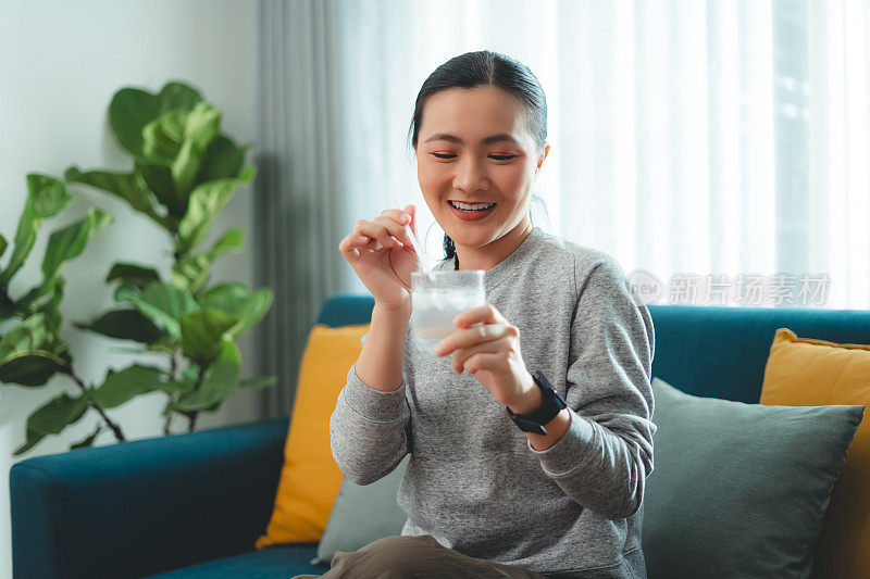 亚洲妇女坐在客厅的沙发上，用稻草搅拌水和冰休息。