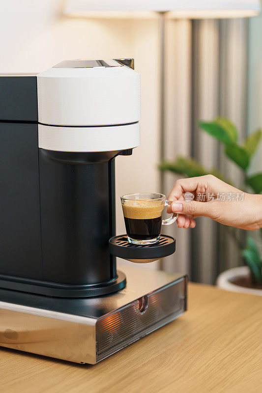 用咖啡机手工制作意式浓缩咖啡，并在木桌上放置烘焙好的咖啡豆胶囊。每日饮品饮品适用于家庭、公寓和办公室的概念