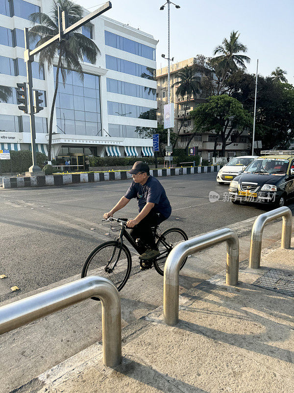 印度马哈拉施特拉邦孟买零售区的主要道路上，一名印度男子骑着自行车与出租车和汽车在一起