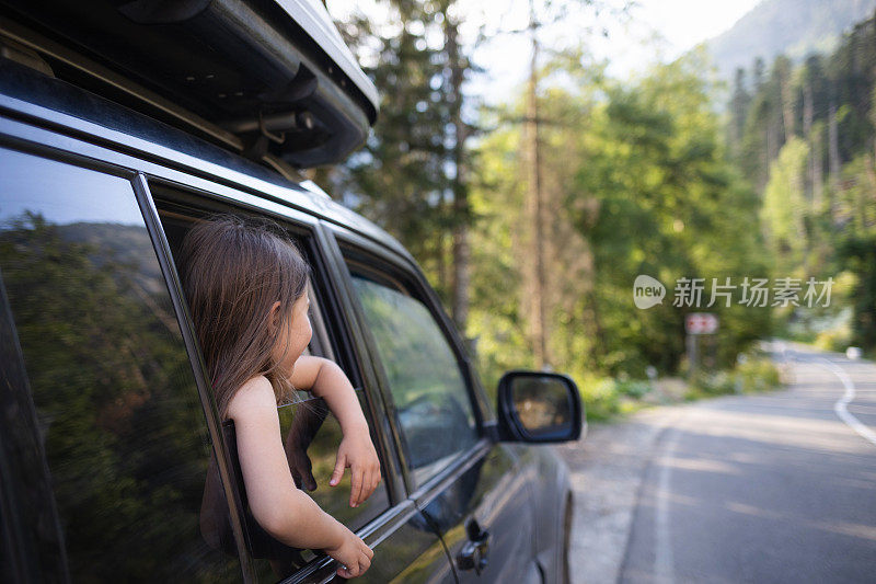 带着孩子开车旅行。小女孩望着车窗外的森林和山路。