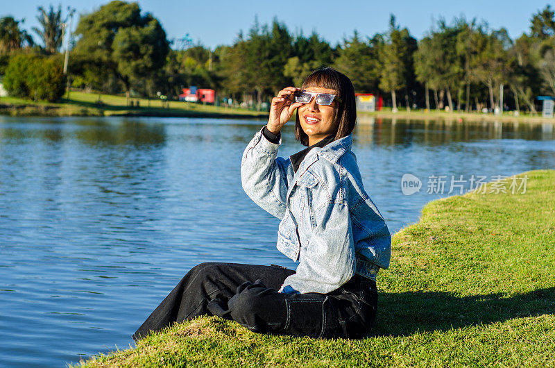 在一个阳光明媚的日子里，一名剪短头发的年轻女子在公园里穿着休闲服，戴着太阳镜