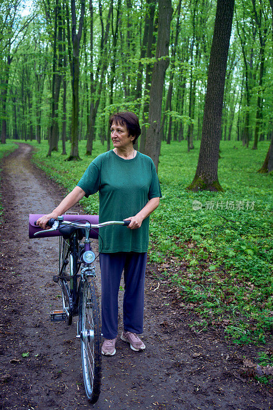 一位老妇人带着自行车和瑜伽垫走在春林里