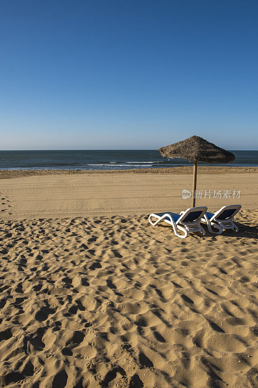 美丽的夏日风景的西班牙海岸，两个太阳躺椅，太阳躺椅和遮阳伞。金色细沙，地平线海景，蓝天，平静放松。鼓舞人心的度假景观。
