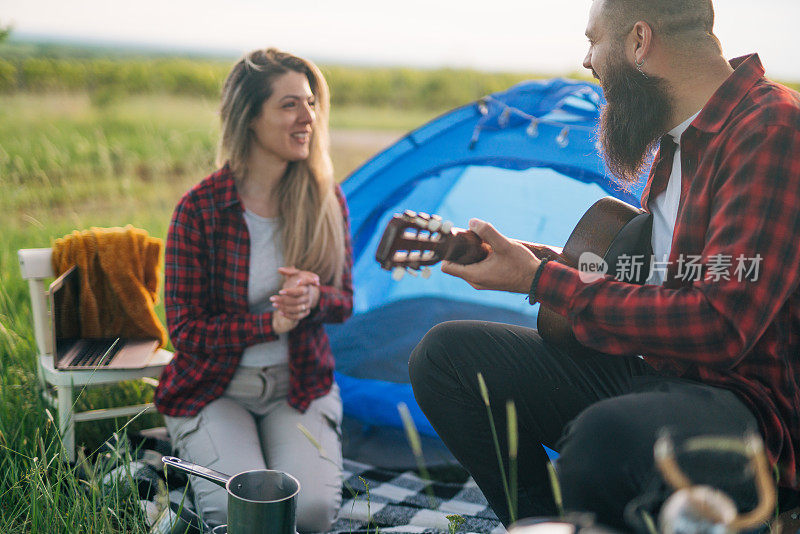 一对年轻夫妇在大自然中露营，一个男人在弹吉他，他们在一起玩得很开心