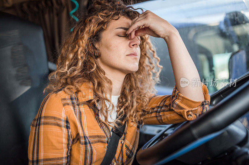 一个疲惫的卡车司机坐在驾驶座上，抱着她的头。她头痛，劳累不堪