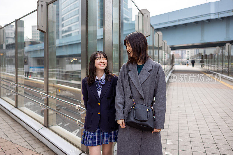 十几岁的女孩穿着校服和她的母亲在城市，看着对方的肖像