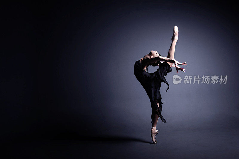年轻的芭蕾舞女演员穿着黑色的衣服在黑暗中跳舞