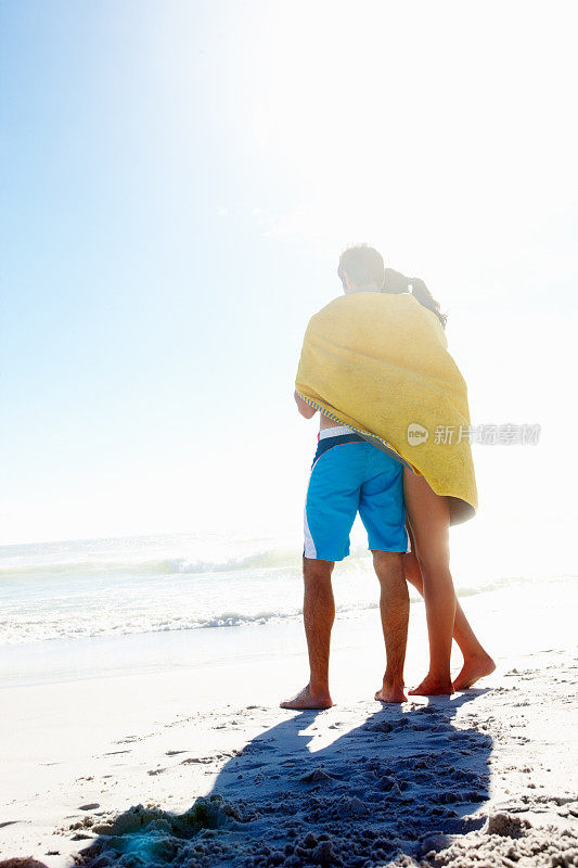 在海滩上，一对深情的夫妇裹着毛巾的后视图