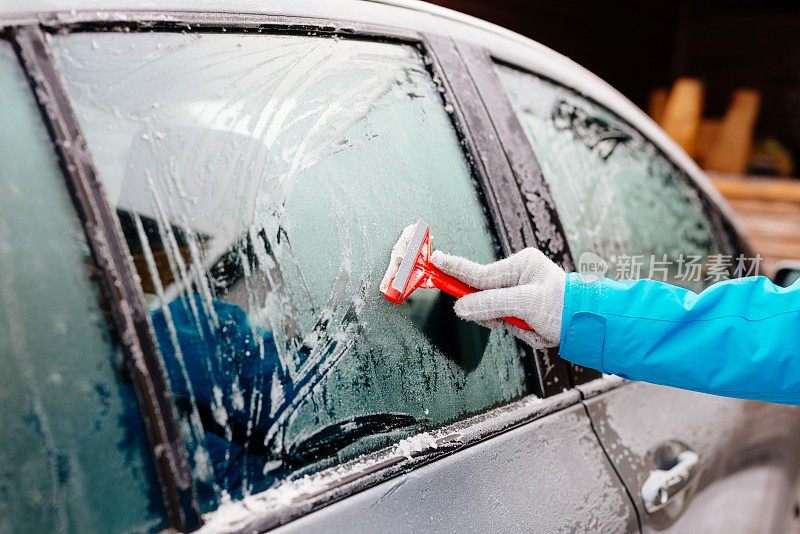 女人用刮刀除冰车挡风玻璃