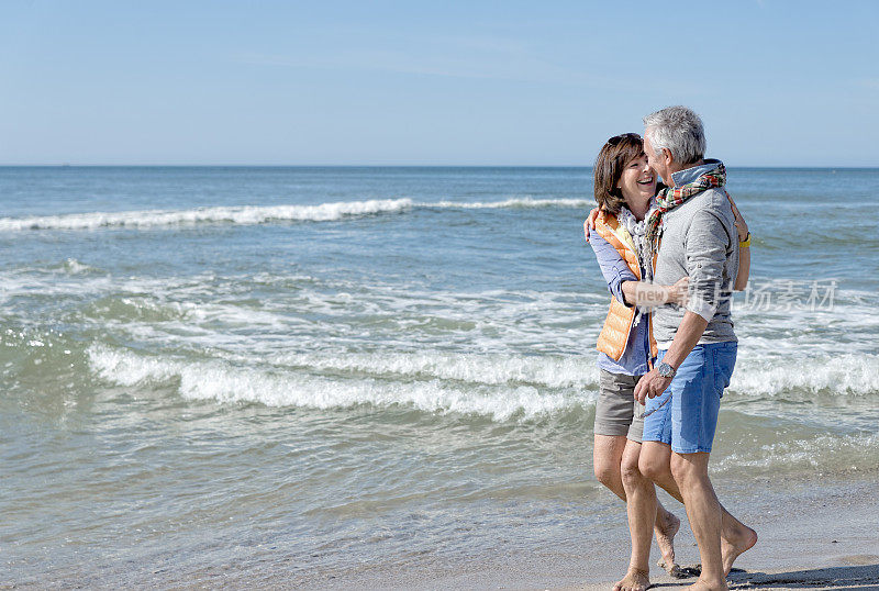 一对大笑的老夫妇在海滩上手挽手散步