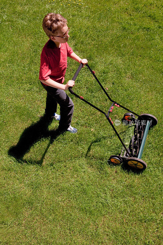 年轻的男孩修剪草坪与非电动推动割草机