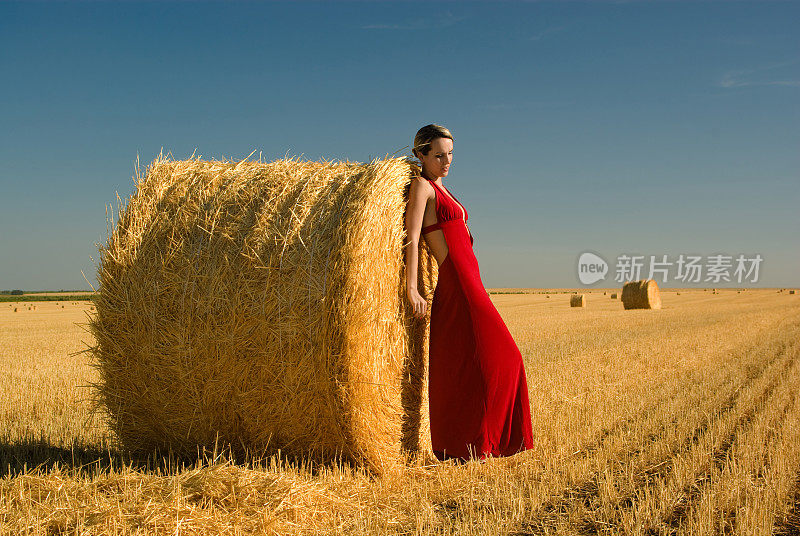 穿着红色晚礼服的女孩倚在稻草捆上