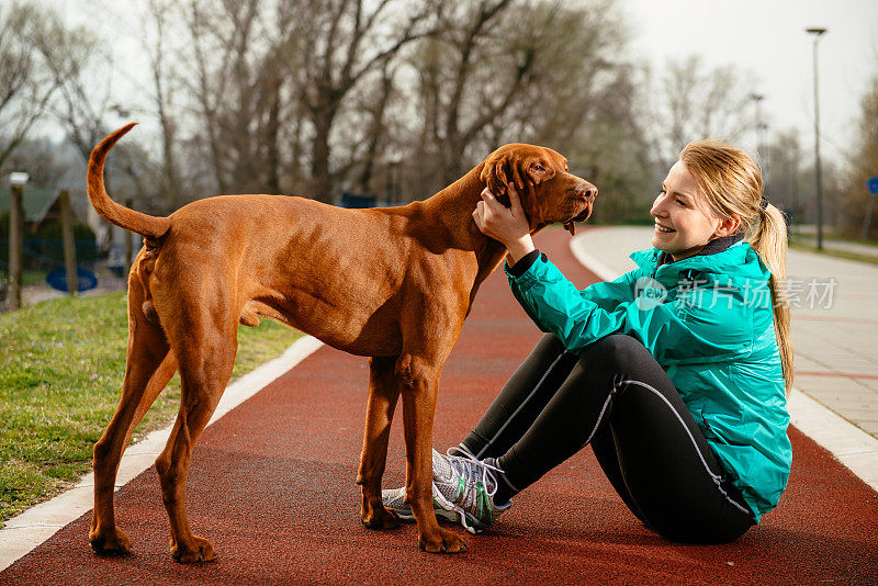 一位年轻女子带着她的狗在田径跑道上慢跑