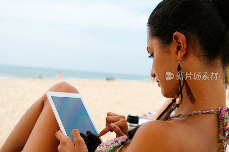 美丽的女孩在沙滩上用平板电脑