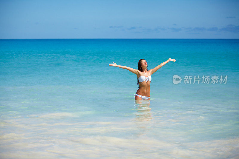 女人在海滩上放松，张开双臂享受自由