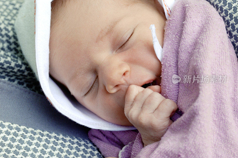 新生婴儿幸福地睡觉，手指在嘴里
