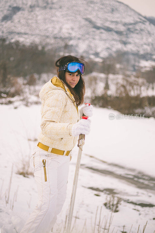 近景美丽的年轻女子在冬天的衣服站在一边，手拿木棍的背景雪山