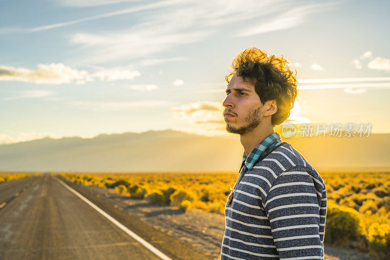 公路旅行。一个年轻人，旅行潮人，在日落时分的内华达州沙漠公路上四处张望