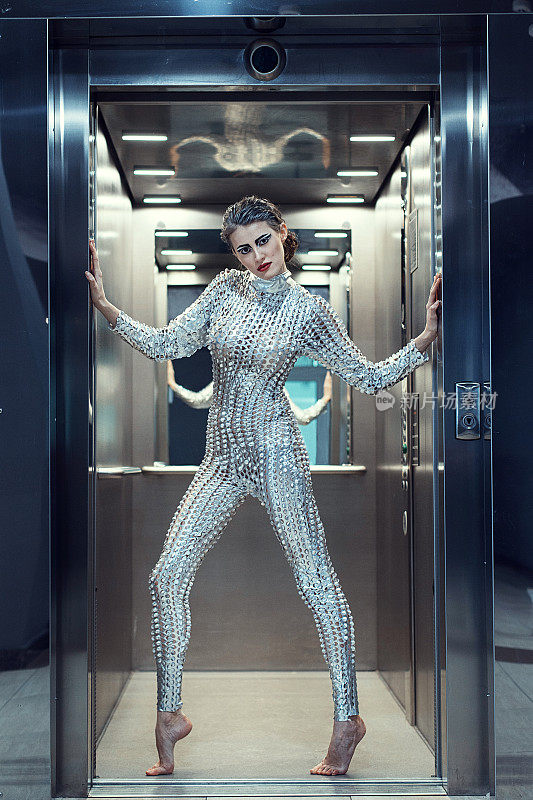 年轻的网络女性穿着银色的未来主义服装站在电梯里。