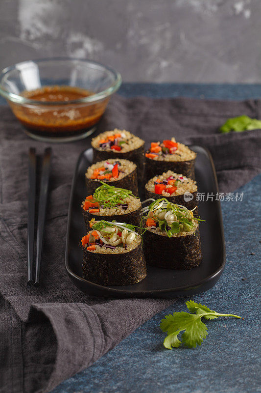 纯素寿司卷配藜麦、蔬菜和豆瓣酱在黑色的盘子上，黑色的背景。素食健康食品概念。