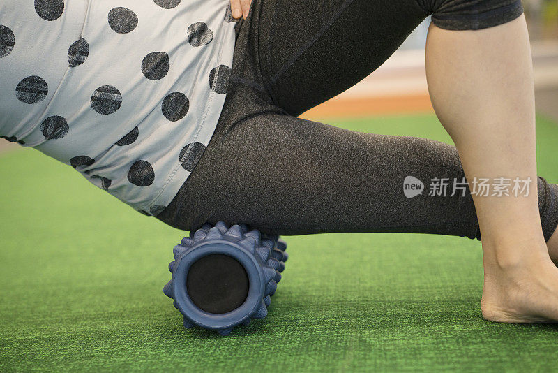 在健身课上，一个女人用泡沫卷在她的腿上来释放紧张和帮助肌肉疼痛