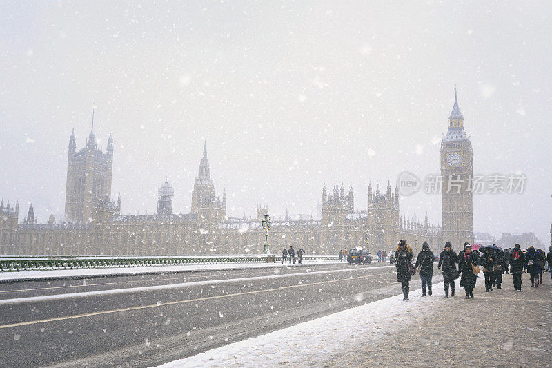 人们在暴风雪中走在威斯敏斯特桥上，背景是英国议会大厦