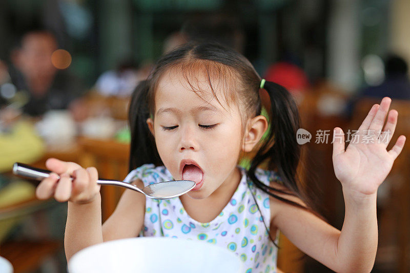 可爱的亚洲女孩用勺子吃粥。孩子吃早餐。