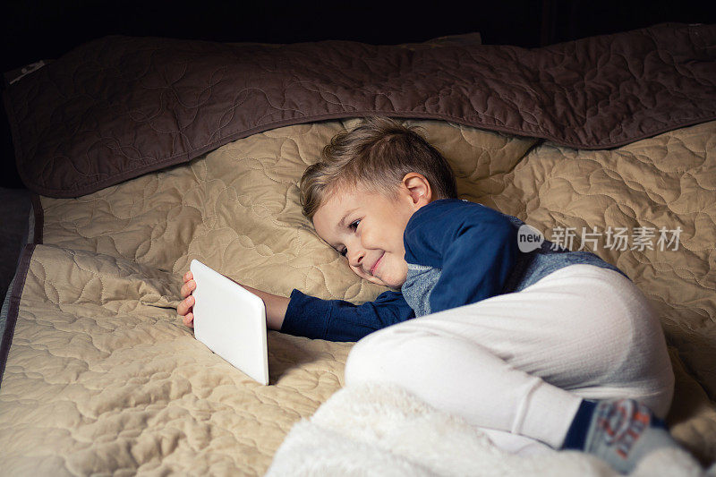 在床上休息时，快乐的孩子在触摸板上看动画片。