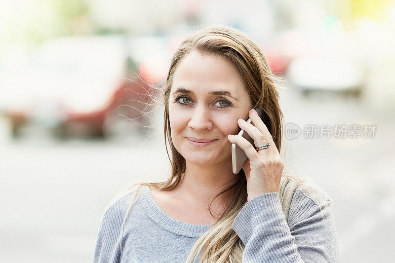 金发美女在街上打电话，对着镜头微笑