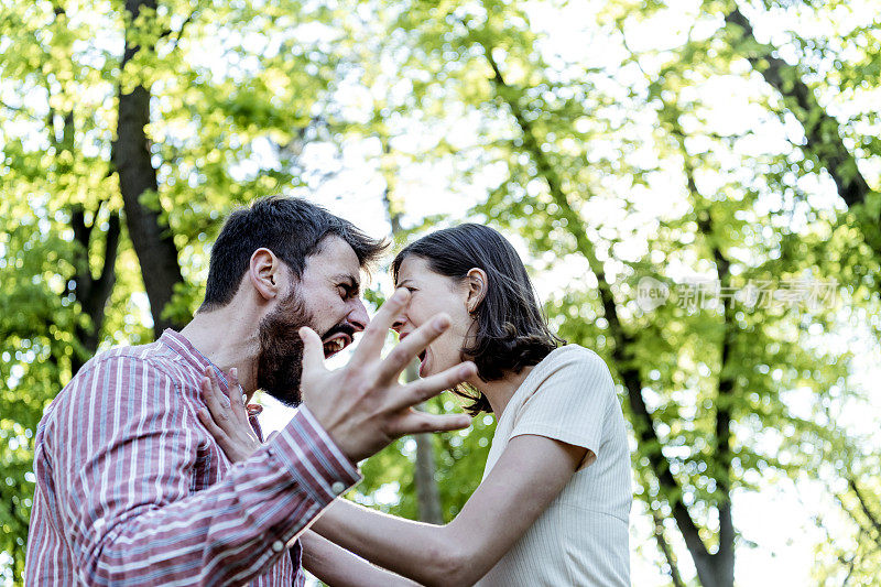 一对年轻夫妇在公园里吵架。年轻夫妇有一个夏天的一天争吵。站在公园外面，困惑的年轻女子打着手势，看着她的男朋友