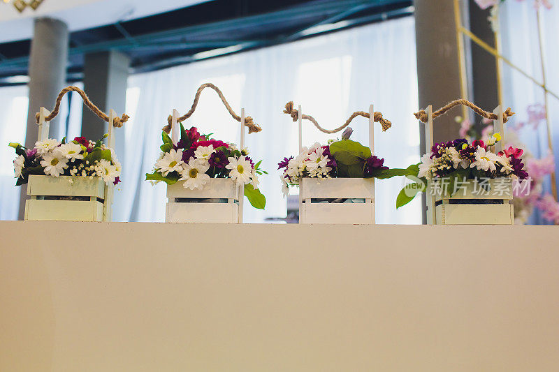 四盆白花摆放在木桌上，屋子里有一扇以散景为背景的窗户。这些花都装在不同形状的花瓶和篮子里。