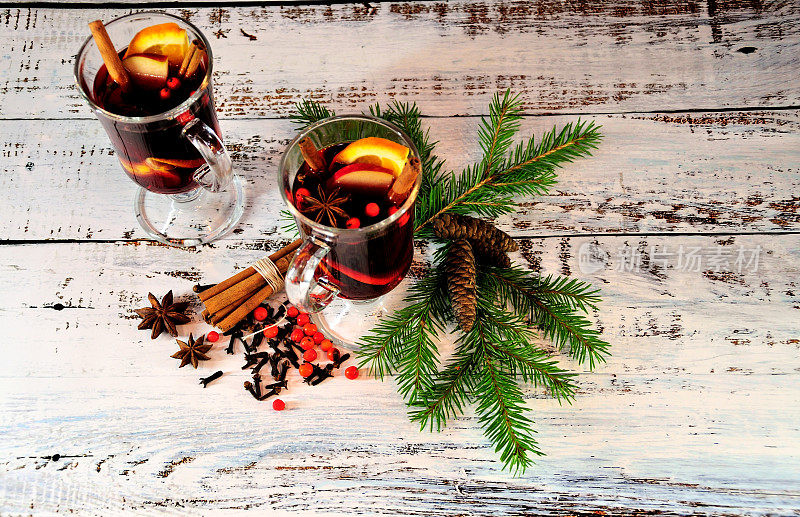圣诞礼物:两杯加肉桂和橘子的热红酒，放在一张桌子上，旁边是冷杉树枝和松果。