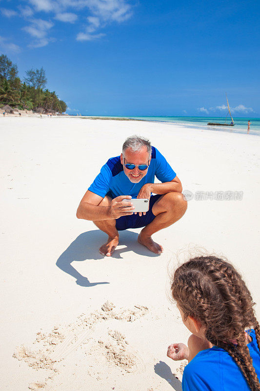 微笑的成熟男子在暑假用手机拍摄他的女儿