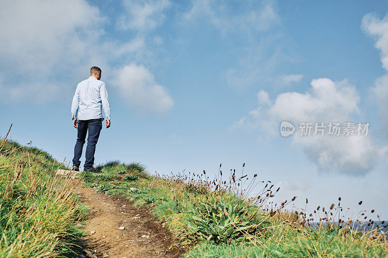 一个阳光明媚的秋日，康沃尔郡纽基市Pentire的男子走在西南海岸的人行道上。