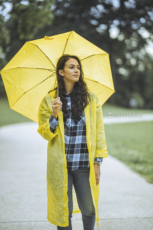 女人穿着雨衣，撑着雨伞，在雨天行走