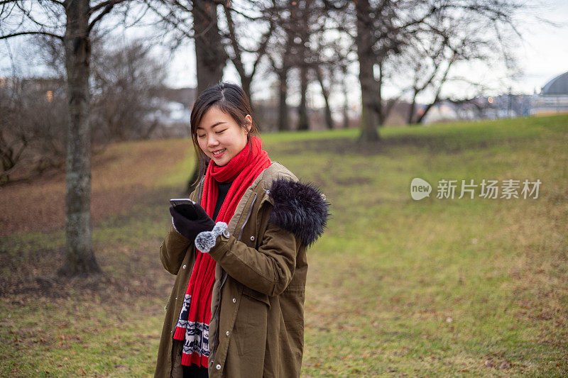 年轻的亚洲女性在温暖的冬天使用智能手机