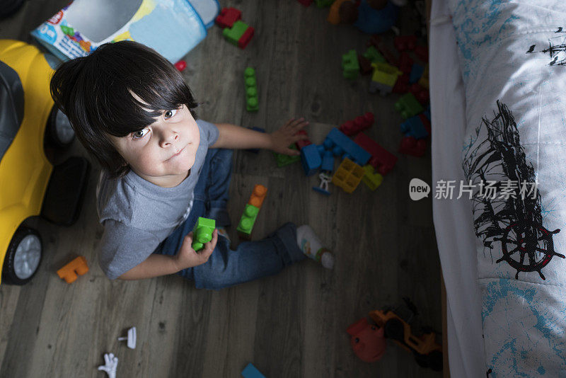 男孩在他房间的地板上玩玩具的时候，看着相机的肖像