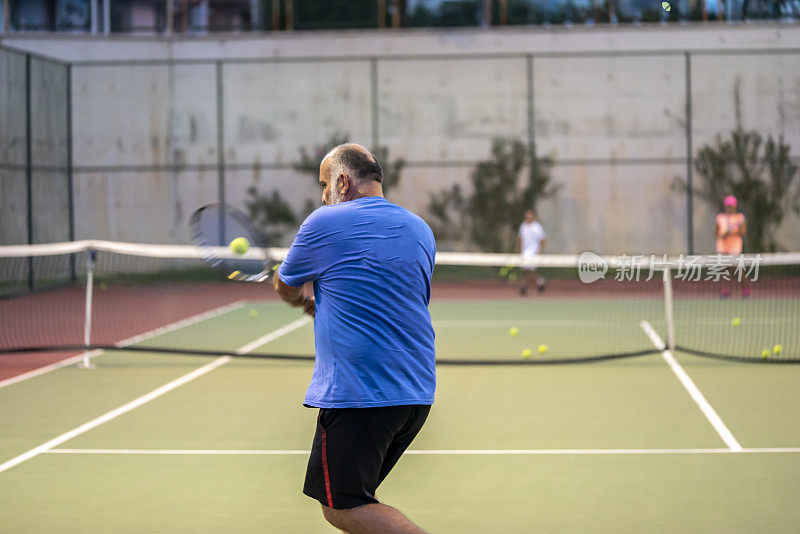 教练正正手击球，让网球选手集中精力在硬地球场的前景上
