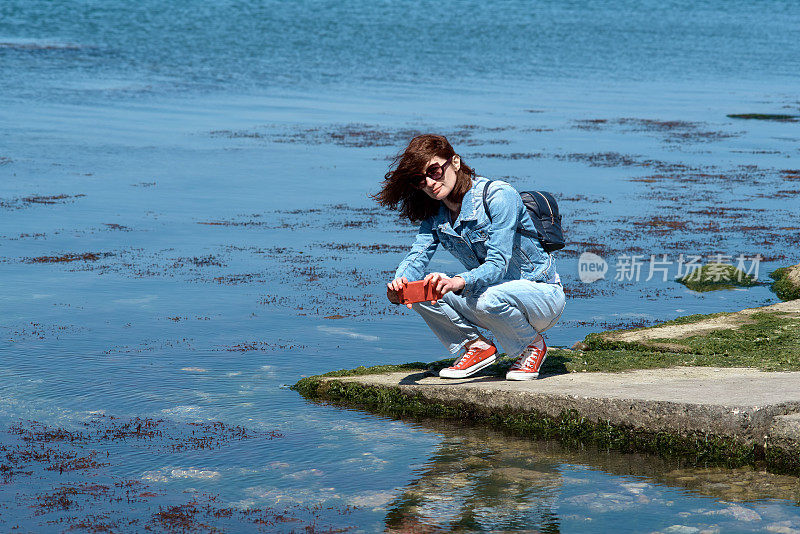 女游客在海边用智能手机拍照