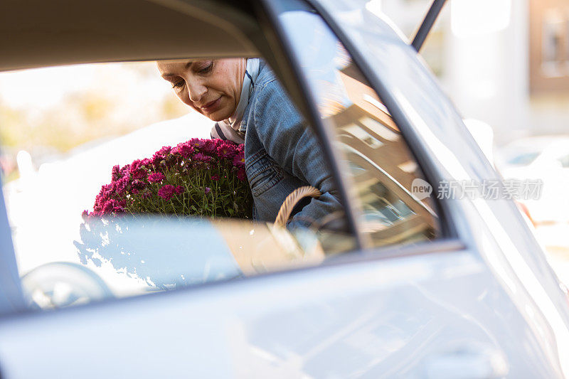 一个女人往她的汽车后备箱装鲜花和杂货