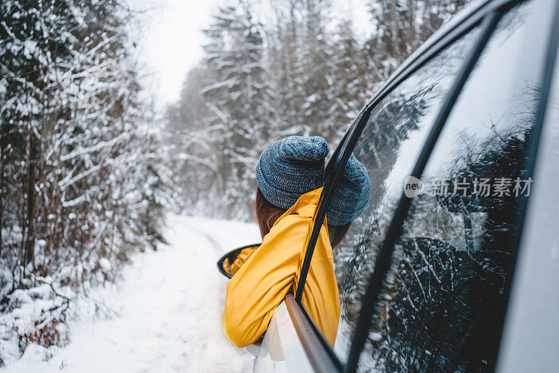 一名女子穿着黄色夹克，望着车窗外，在冬天的森林里旅行。时髦女孩欣赏雪道。游客们在美丽的冬季景色中休息