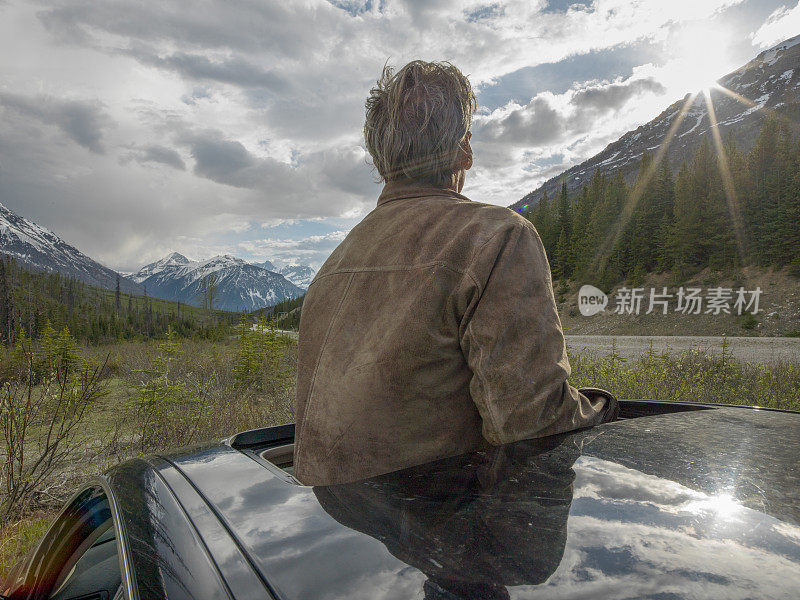 在山路上，一个男人穿过汽车天窗站起来