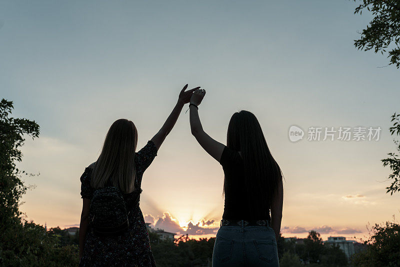 夕阳背景下的两个女孩。最好的朋友。日落时分，两个女人手牵着手